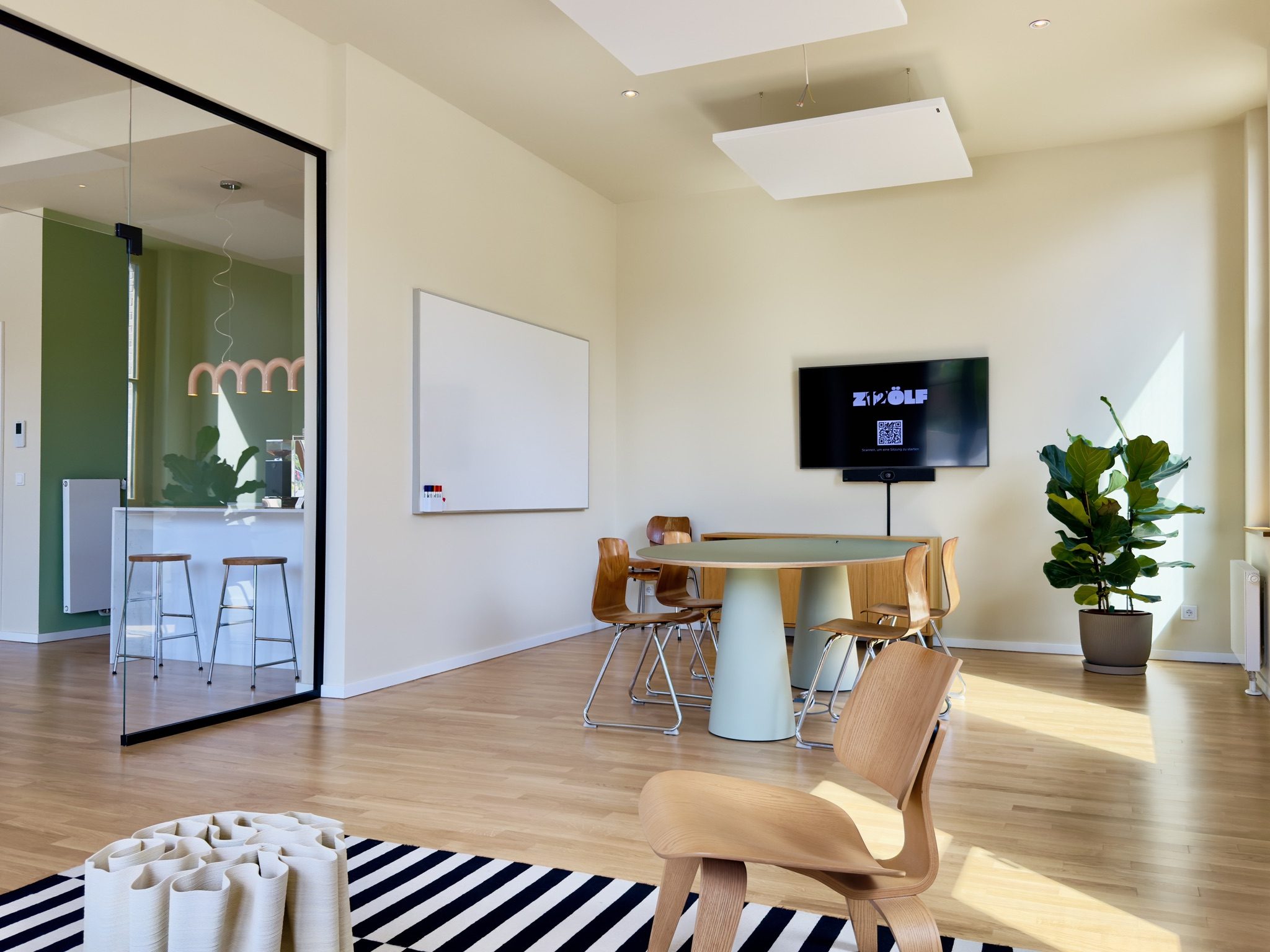 Heller Hauptraum mit rundem Tisch, Whiteboard und Blick in die offene Küche